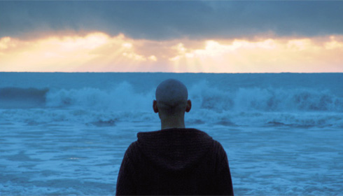 View from the back of the a man looking over surf and out to sea from the film, Un Buda by Diego Rafecas.
