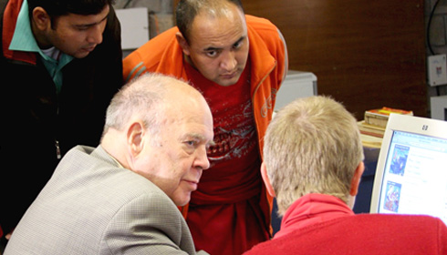[seated Gene Smith listening to man in front of computer monitor with two men looking on]