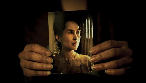 woman's hands hold up a color photo of Aung San Suu Kyi