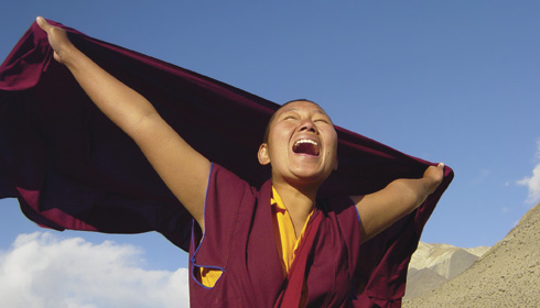 [joyful young nun extends arms overhead as wrap blows in the wind]