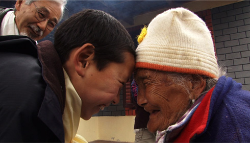 [young Tibetan boy and old Tibetan woman smile and press foreheads in greeting]