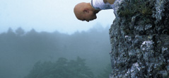 [man with shaved head suspended out over mountain side]