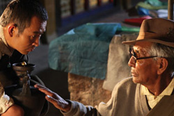 [young man holding pottery looks towards older man with glasses and hat and hand extending to touch pottery]
